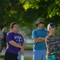six adults standing outside in the sun listening